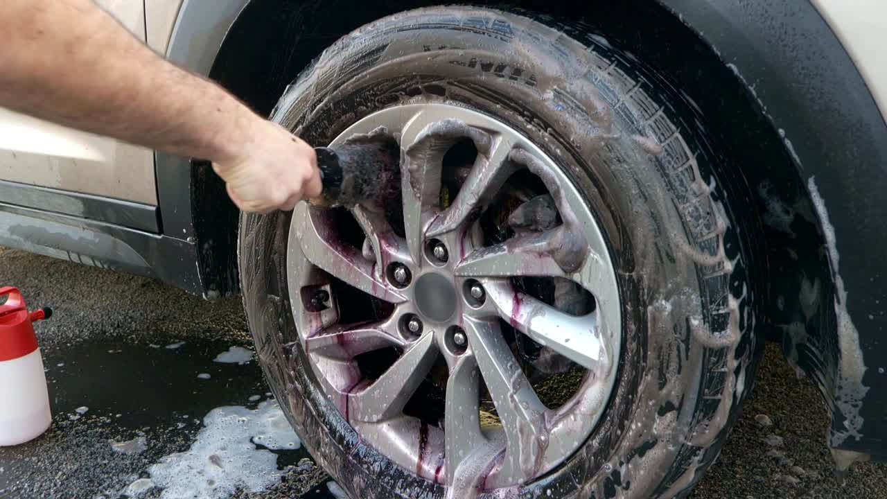 Medium shot of cleaning SUV alloy wheel with red and black barrel brush