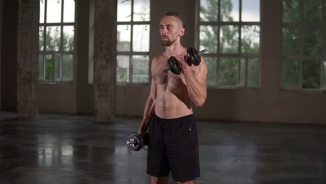 hombre musculoso sin camisa haciendo ejercicio con pesas y sudor en su cuerpo. hombre sin camisa con torso sudoroso haciendo ejercicio en un estudio de loft vacío. cámara lenta