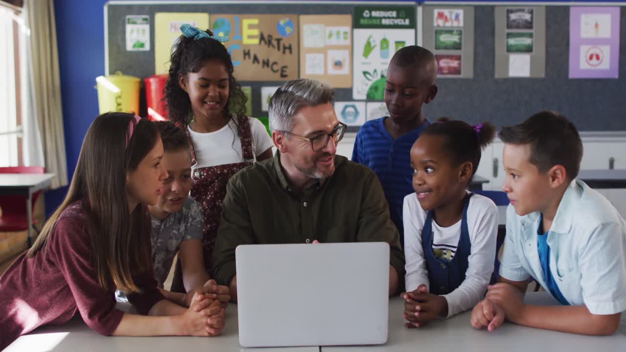 Diverse male teacher and group of schoolchildren looking at laptop