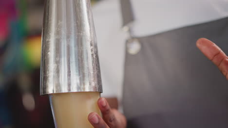 bartender pours cocktail into glass from shaker in bar closeup. african american barman serves alcohol drink in nightclub. black man prepares beverage