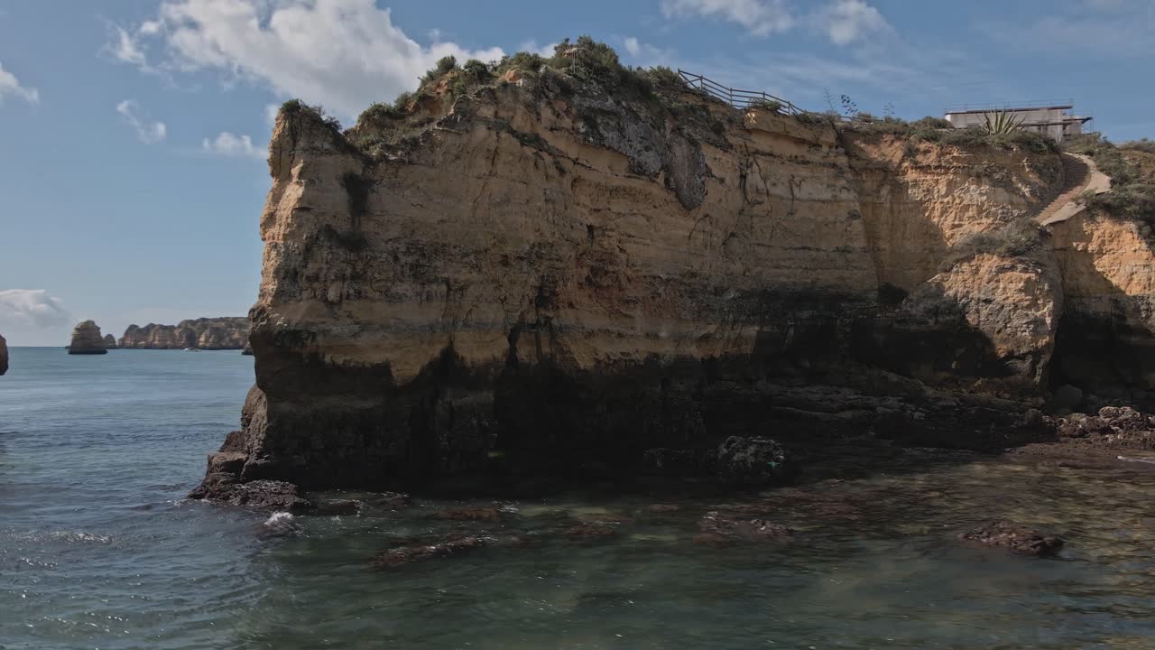 Aerial drone performs a helix orbit around dramatic limestone sea arches and layered cliffs, with water sparkling in the sun near Lagos, Algarve, Portugal