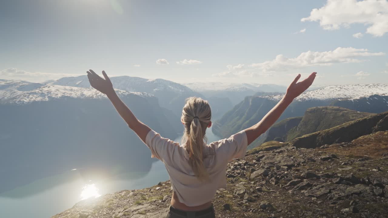 una mujer joven saluda a la naturaleza con los brazos abiertos en la caminata del monte prest en noruega