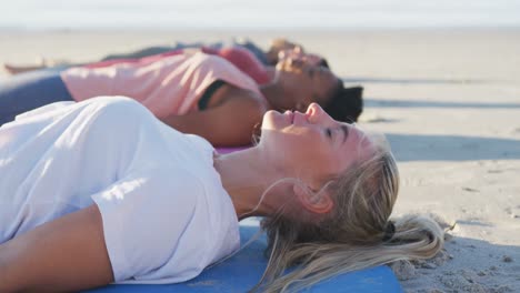 un groupe d'amies diverses pratiquant le yoga, allongées sur des tapis sur la plage