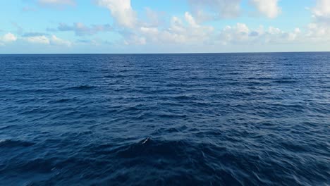 Dolly-Aéreo-Bajo-Vuela-Paralelo-Sobre-El-Agua-Azul-Profunda-Del-Caribe-Con-Nubes-Esponjosas-En-La-Distancia