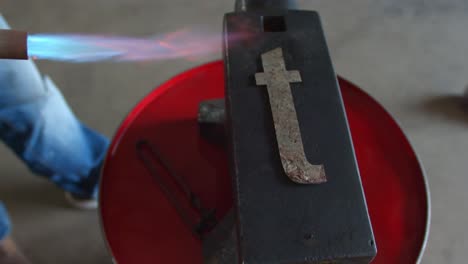 blacksmith forging a metal letter t