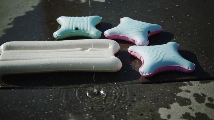 Goccia che colpisce creando un'onda su una piastrella a bordo piscina, con un lettino bianco e cuscinetti a stella che mostrano scie.