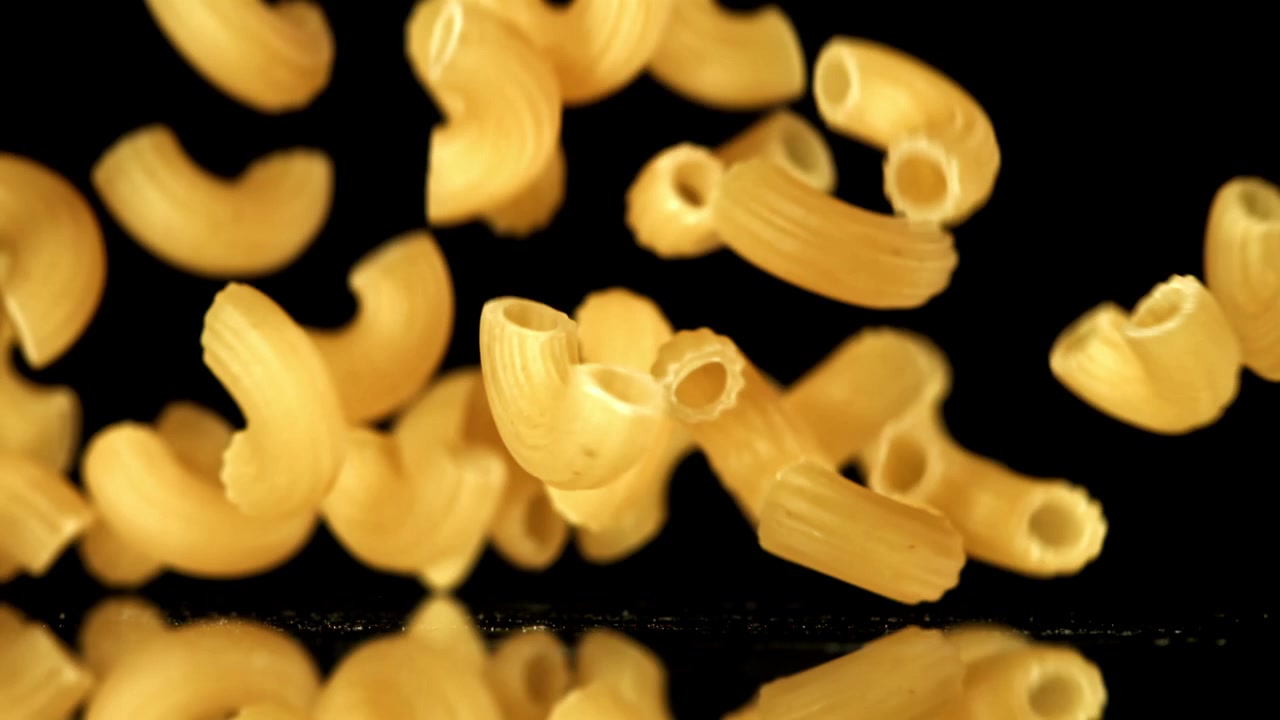 Pasta maccheroni secca che cade al rallentatore su sfondo nero.