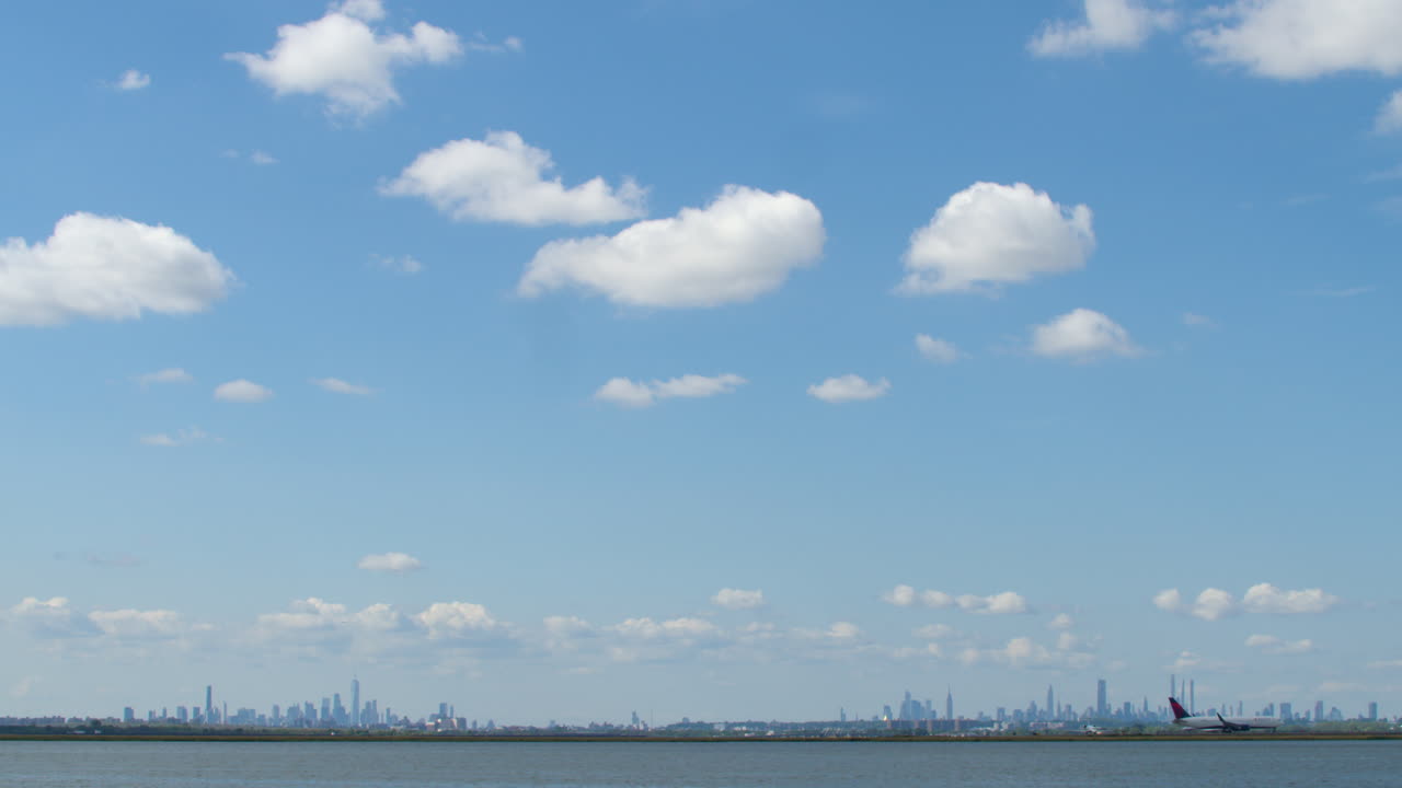 Commercial Jet Crosses Frame Against Bold Blue Sky on Approach to Kennedy Airport with Manhattan Skyline Sitting Low on Horizon