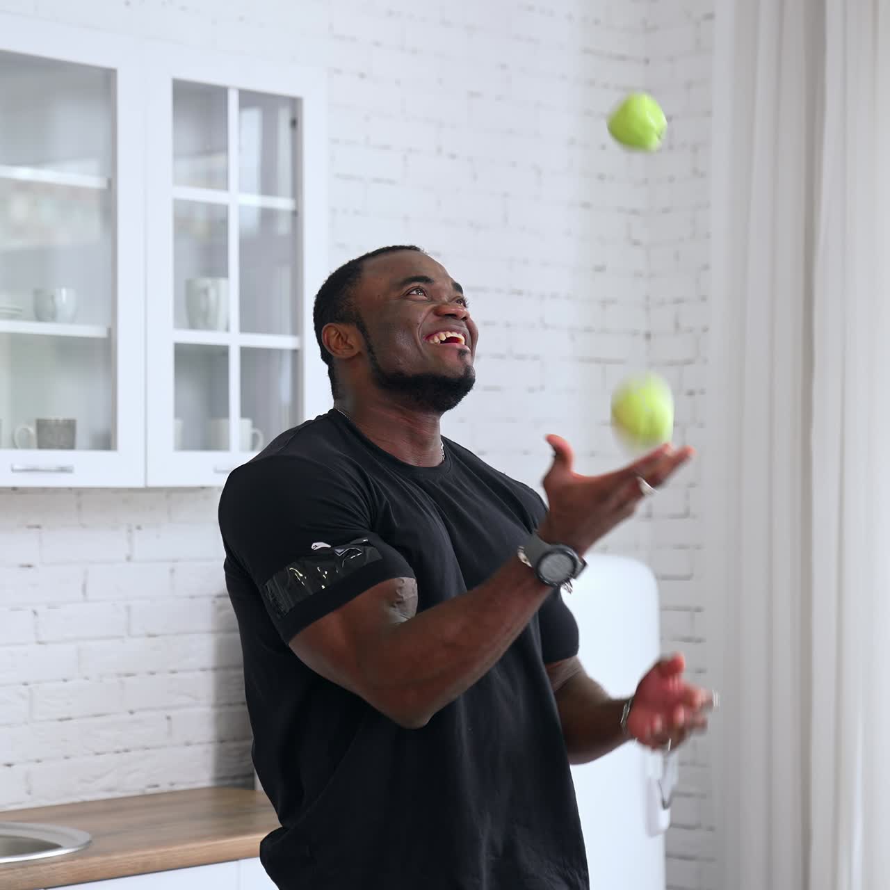 Happy young multiracial man joggling apples in kitchen background, selective focus, closeup. Dieting concept. Healthy man throwing up fruits