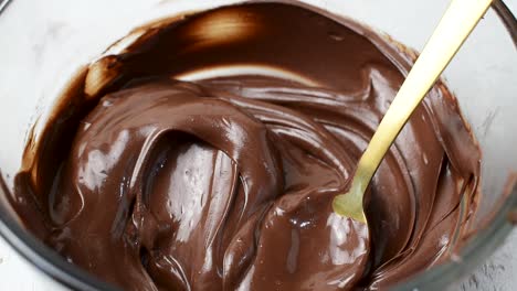 stirring melted chocolate with spoon in glass bowl and dipping strawberry