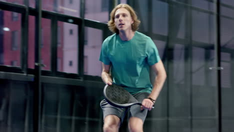 playing padel tennis, man focused on returning ball in indoor court