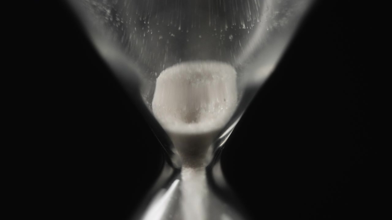 White Sand Running Through a Glass Hourglass on Black Background