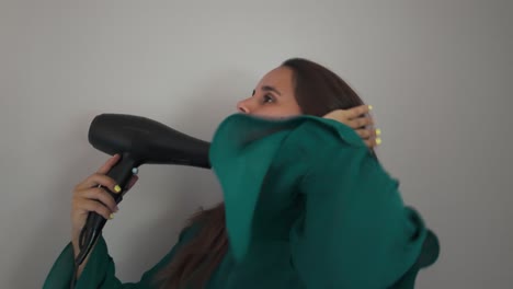 girl blow-drying her hair indoors waving her hand through long brown hair as she drapes it over shoulder