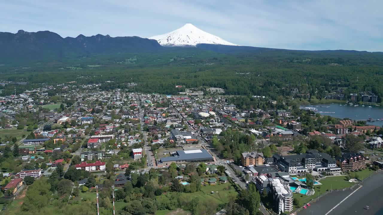Drone shot flying backward over Pucon with stunning view of the town, lake and Villarrica Volcano in the background on a clear day