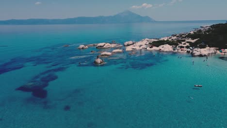 Aerial-flyover-Beach-of-Kavourotrypes-at-Chalkidiki,-Greece-with-many-people-jumping-into-clear-blue-water