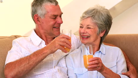 senior couple sitting on couch having orange juice