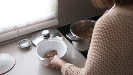woman plating meat with sauce in a kitchen