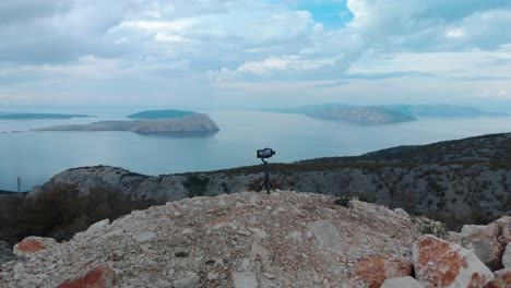 arc shot around phone and gimbal place on a rock above the seashore in cloudy day