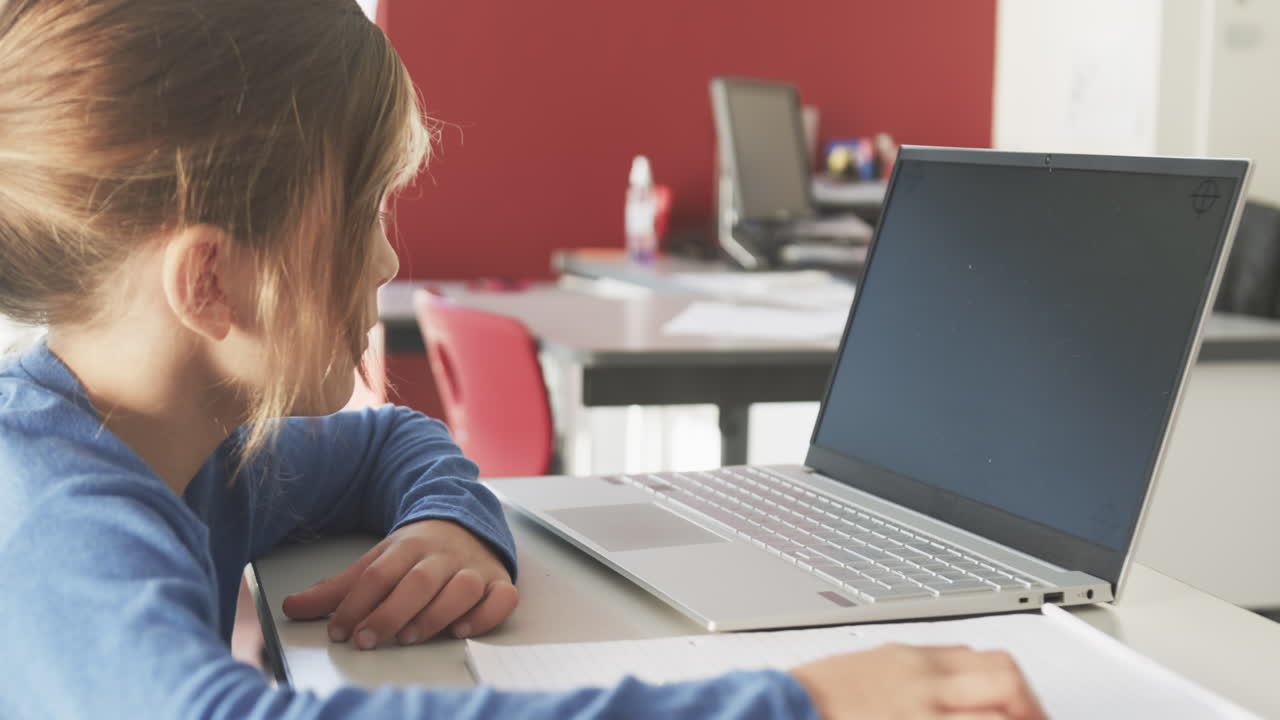 In school, boy using laptop and writing in notebook, focusing on work, copy space