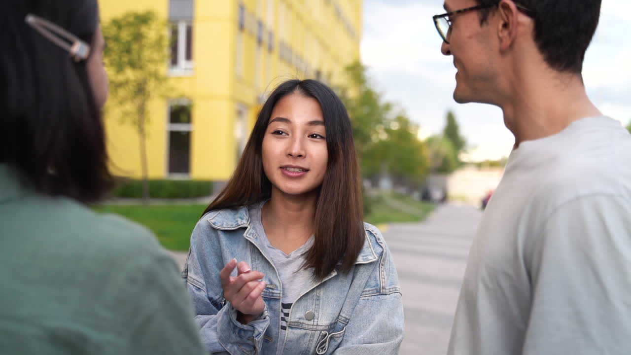 grupo de tres felices jóvenes amigos japoneses parados afuera y hablando entre ellos 1