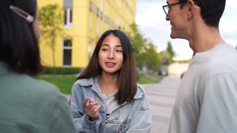 group of three happy young japanese friends standing outdoors and talking to each other 1