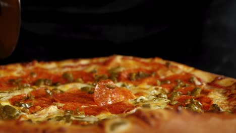 close-up hand slicing the salami pizza into slices using a roller pizza cutter