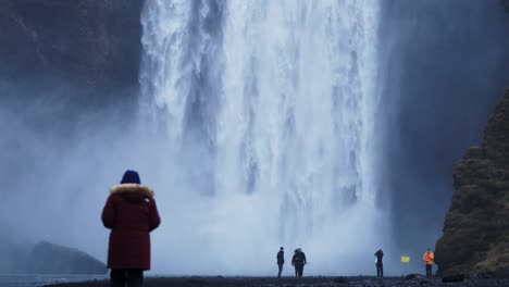 Turista-Visitando-La-Cuenca-De-La-Poderosa-Cascada-Skogafoss-En-Islandia