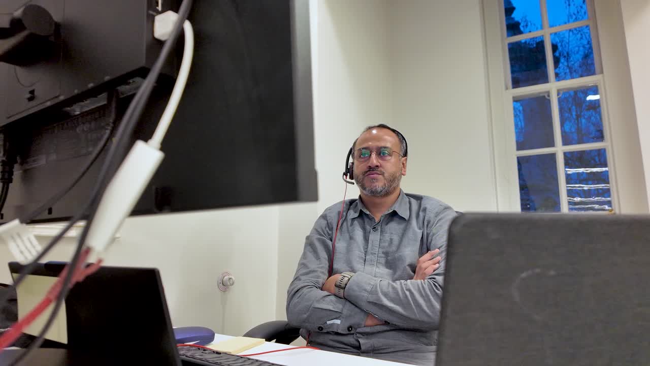 Uomo dell'Asia meridionale che lavora alla scrivania con laptop e monitor, indossa una cuffia in ufficio, seduto su una sedia girevole con le braccia incrociate per concetti di business o assistenza clienti