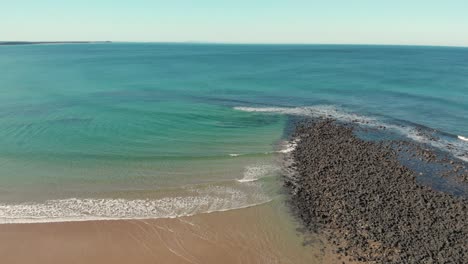 AERIAL-DOLLY-BACK-Black-Volcanic-Rocks-Along-A-Sandy-Beach