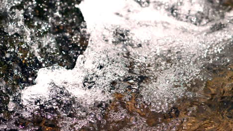 burbujas de agua emergen de un arroyo en la base de una cascada filmada en cámara lenta