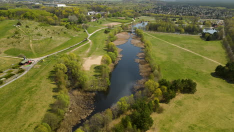 Aerial-flyover-beautiful-park-named-Myślęcinek-with-lake,trees-and-paths-for-walk-during-sunlight