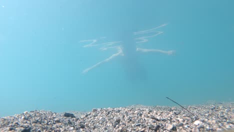 Man-swimming-throuch-ice-cold-clacial-water---Underwater-static-shot-looking-up-from-bottom-and-watching-man-swimming-past-camera---Beautiful-light-rays-penetrating-through-water-surface---Loen-Norway