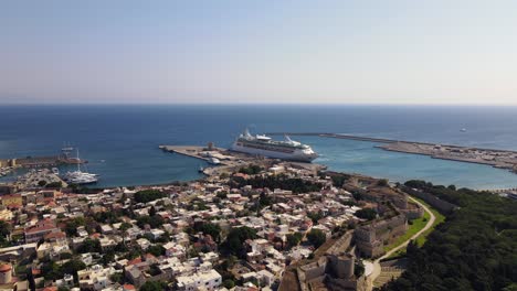 drone flies over the old town of rhodes towards a docked cruise ship in the kolona harbor