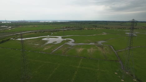 Vista-Aérea-Ascendente-Sobre-Torres-De-Pilón-De-Distribución-Eléctrica-En-Campo-Inundado