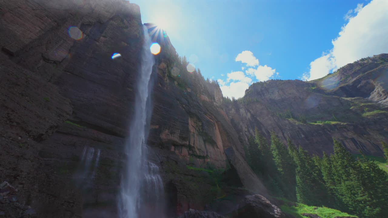 Sunny mist Telluride Bridal Veil Falls Waterfall Black Bear Pass Road Colorado landscape pan down motion spray Ouray Ridgway Box Canyon cliffside hydropower house 4wd hiking blue sky boulders creek
