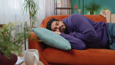 tired indian man lying down in bed taking a rest at home napping falling asleep on sofa relaxing