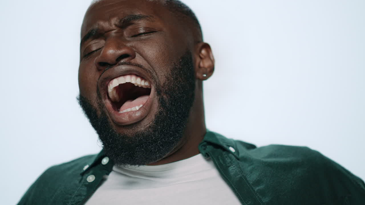 Closeup bored african male person yawning at camera in light background.