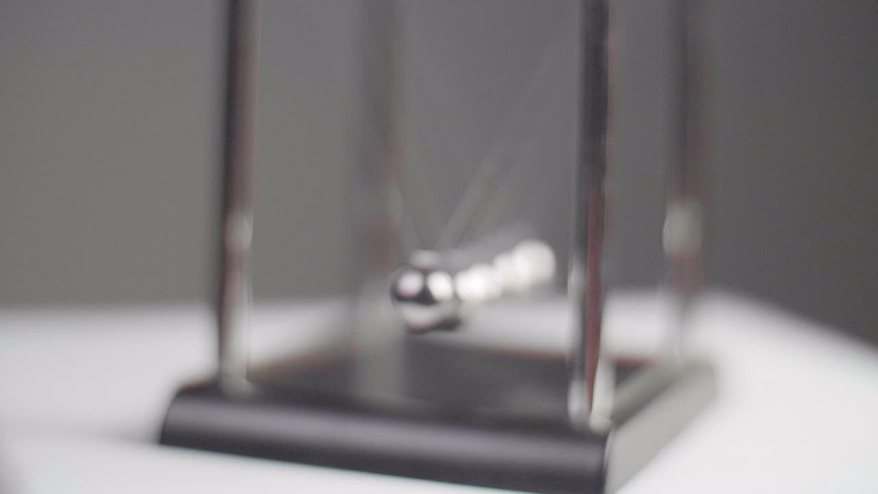 Slow motion: Newton's cradles swinging on a white minimal surface with a dark background in Slow Motion. Camera dolly movement with fixed focus and shallow depth of field. Shot in 4K.