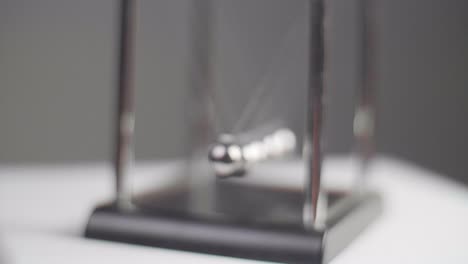 slow motion: newton's cradles swinging on a white minimal surface with a dark background in slow motion. camera dolly movement with fixed focus and shallow depth of field. shot in 4k.
