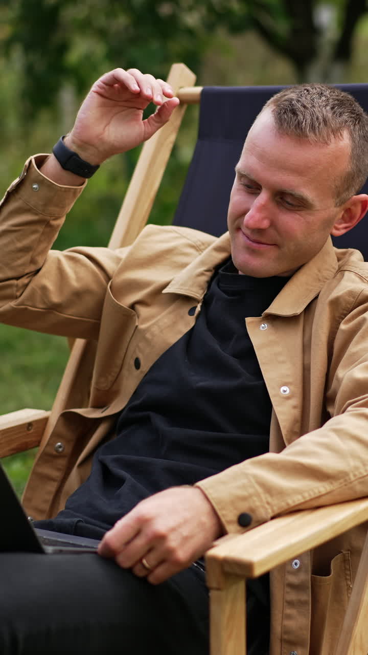 Handsome man with laptop in garden working. Relaxing with notebook. Vertical video