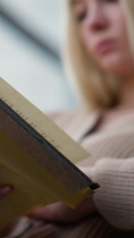 primer plano de una joven leyendo un libro mientras pasa a la siguiente página, sentada en un entorno acogedor, centrarse en las manos sosteniendo un libro desgastado, expresión pensativa borrosa
