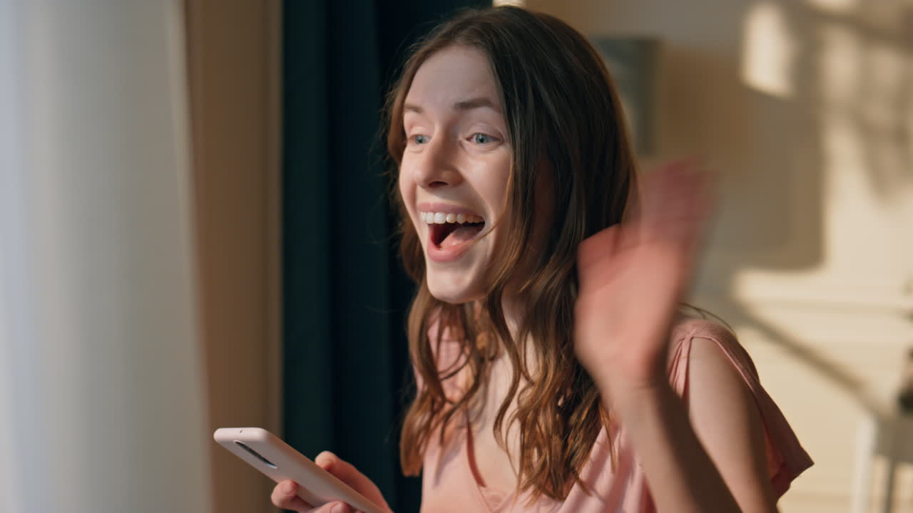 클로즈업 소녀가 집에서 드폰으로 문자 메시지를 보내고 있다. 흥분한 여자가 창문을 바라보며 손을 흔들고 있다.