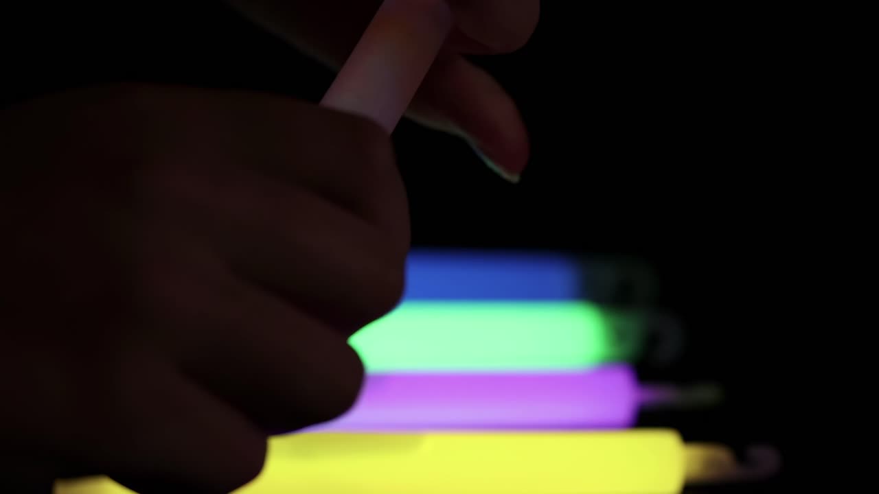 Close-up of hands arranging colorful glow sticks against a dark background, showcasing vibrant neon colors.