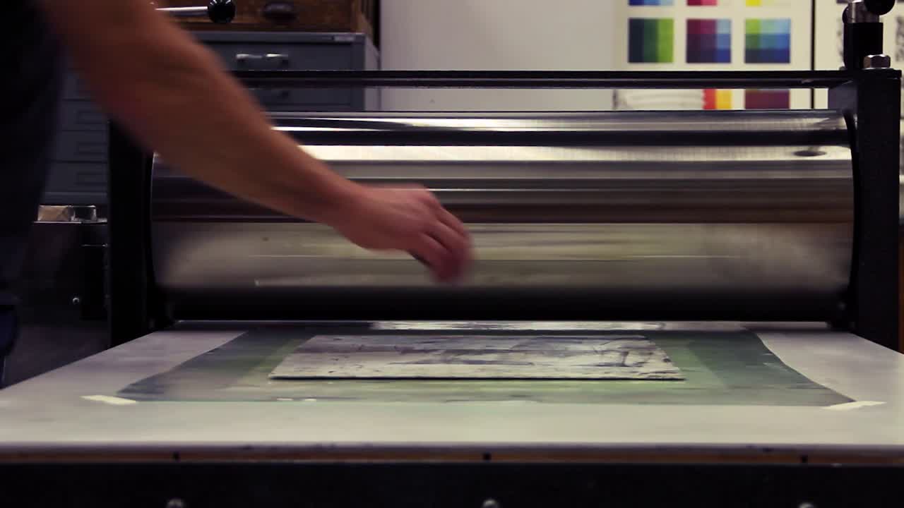 Running a woodblock print through a printing press.