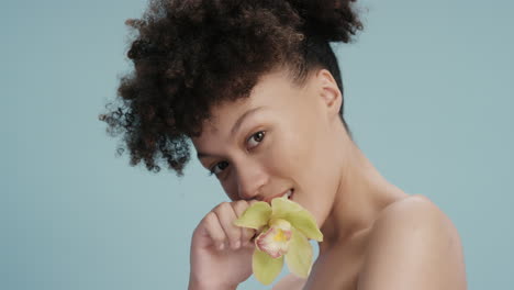 Primer-Plano-Retrato-Hermosa-Mujer-Joven-Tocando-La-Piel-Con-Flor-De-Orquídea-Acariciando-Una-Tez-Suave-Y-Saludable-Disfrutando-De-Una-Fragancia-De-Belleza-Natural-Sobre-Fondo-Azul-Concepto-De-Cuidado-De-La-Piel