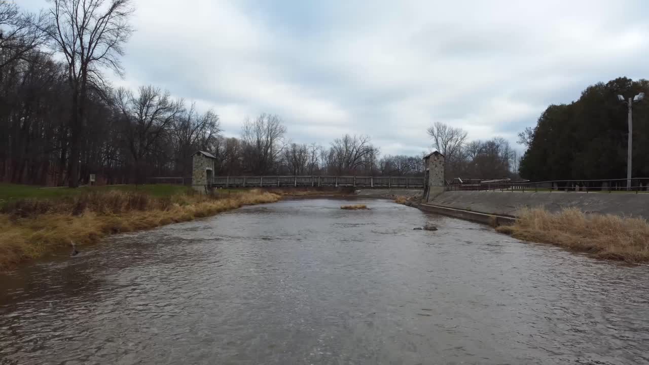 An aerial shot of rustic bridge in a forest and park overlooking river during the fall