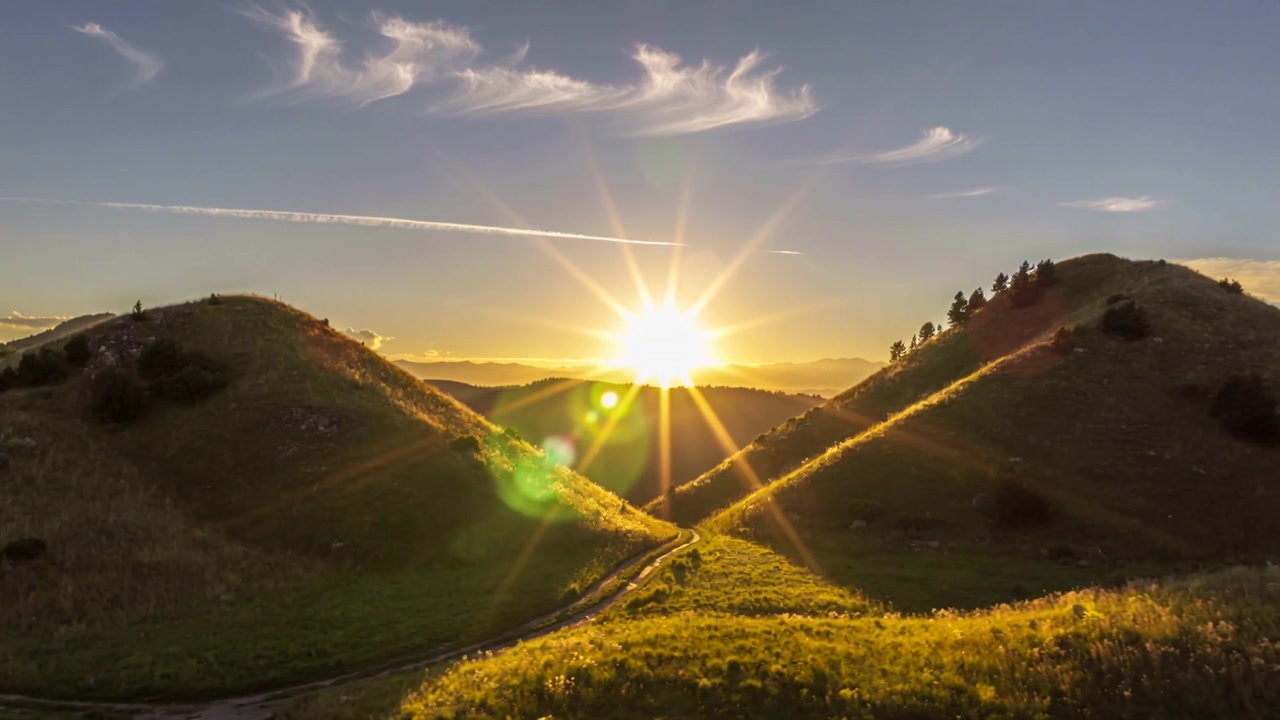 Sol naciente cruzando el horizonte enviando un destello de estrella y un destello de lente verde sobre una colina cubierta de hierba, iluminando el camino.