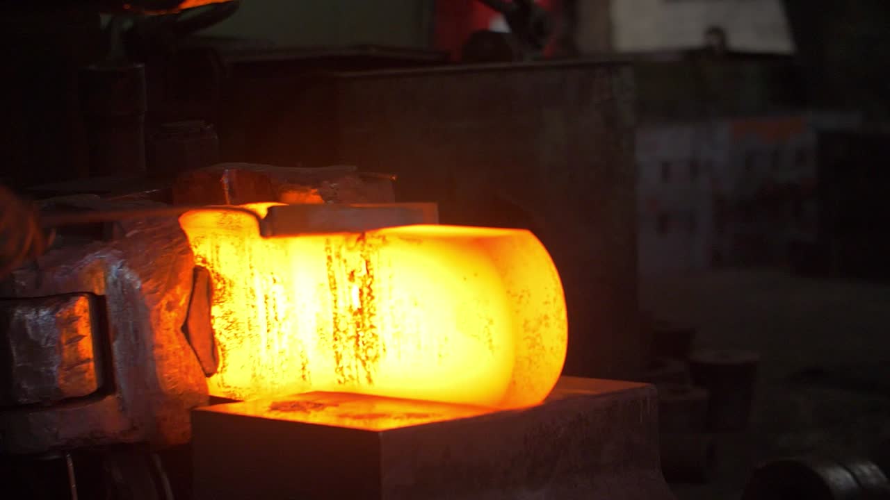 Fabbro che taglia metallo caldo con martello automatico e coltello industriale nello stabilimento.