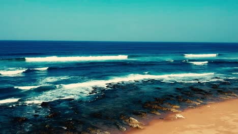 Luftaufnahmen,-Die-Mit-Einer-Drohne-Gefilmt-Wurden,-Mit-Blick-Auf-Den-Strand-Und-Das-Meer-Aus-Tosenden-Wellen-Mit-Einem-Tiefblauen-Ozean-Auf-Der-Klippe-In-Der-Südlichen-Hemisphäre-Afrikas