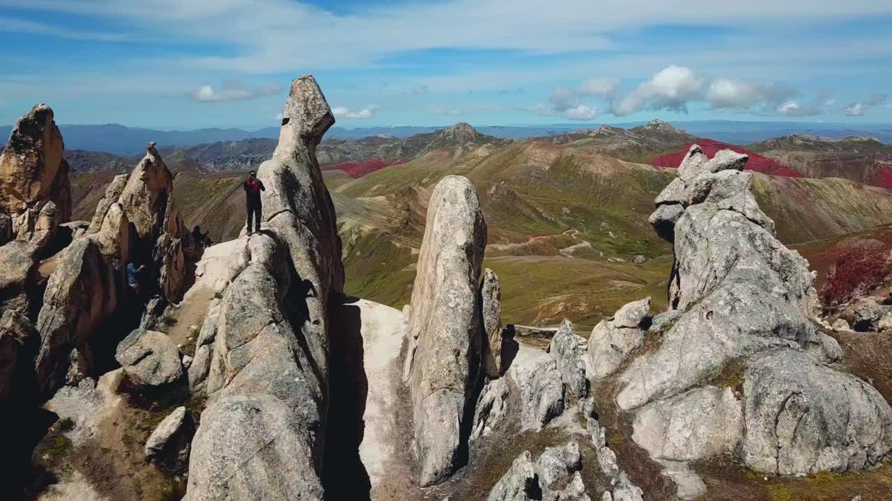 Aerial, orbit, drone shot around a man standing on huge rocks, at the Palcoyo rainbow mountain, in Valle Rojo Valley, Andes, Peru, South America